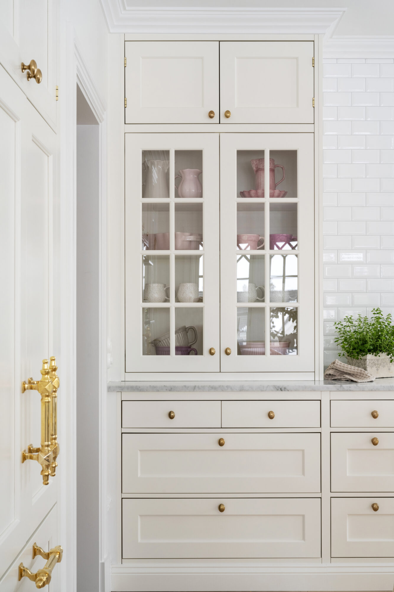 Vitt vitrinskåp med glasluckor och mässingsbeslag