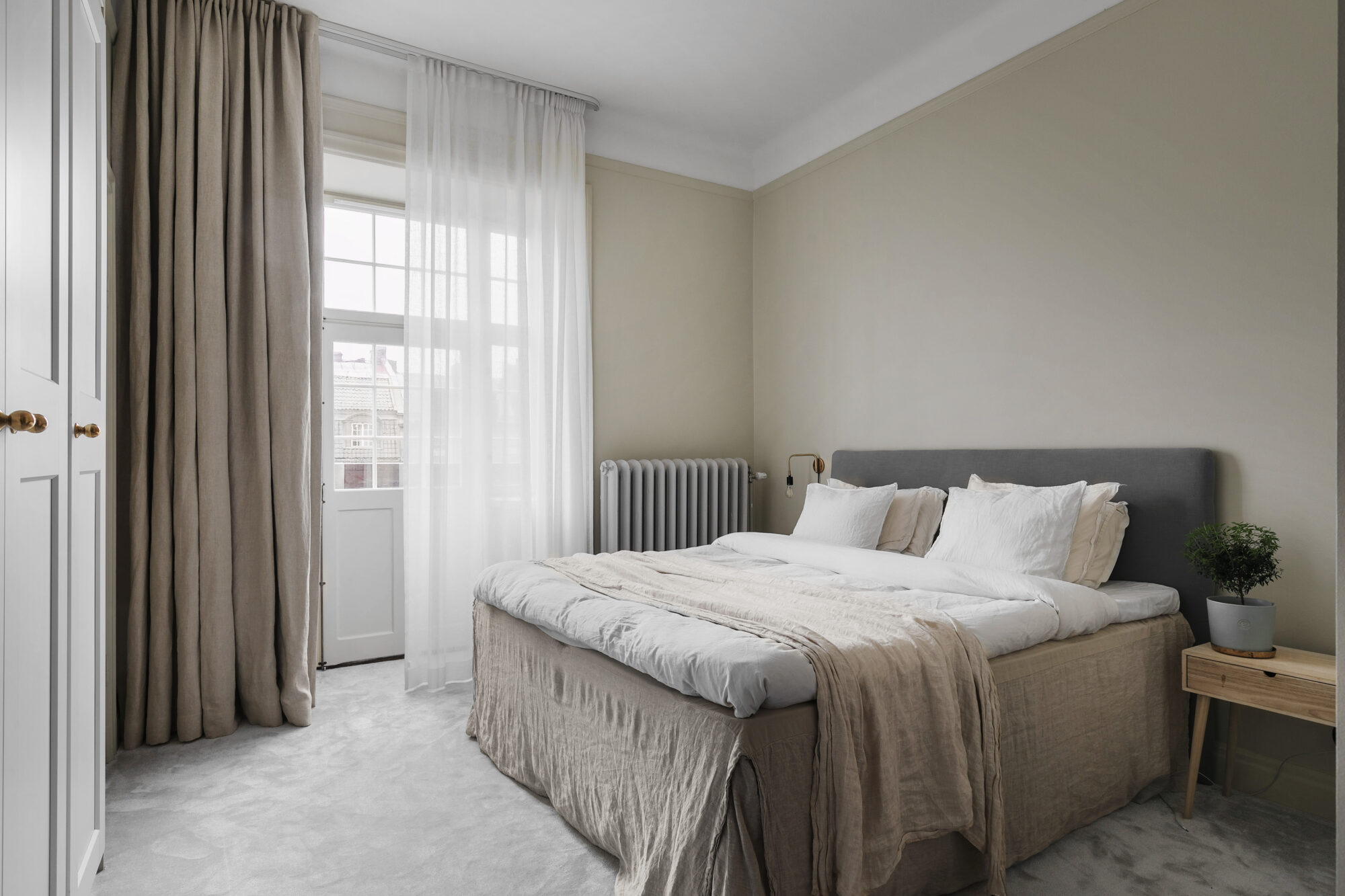 Sovrum i sekelskifteslägenhet med ljusa textilier och höga fönster